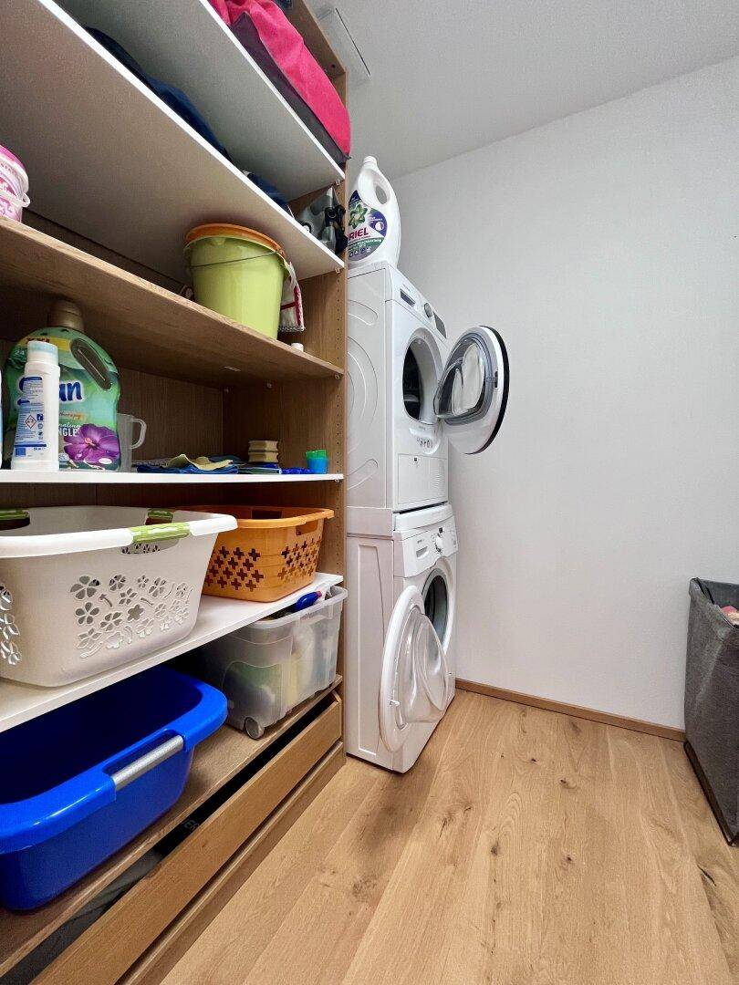 Hauswirtschaftsraum mit Waschmaschine, Trockner und Regalen für Lagerung.