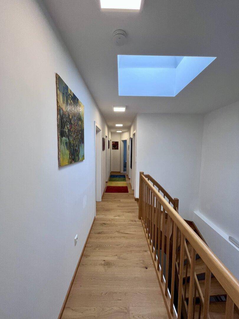 Heller Flur mit Holzboden, Oberlicht und Kunst an der Wand.