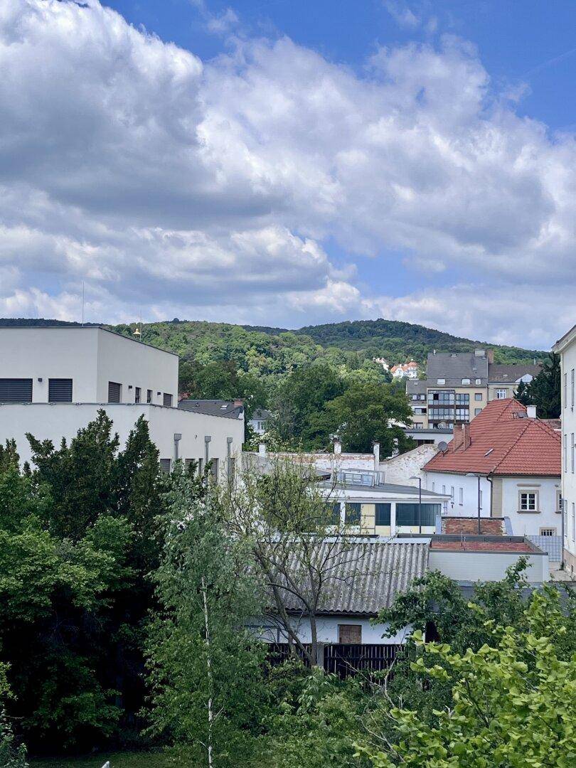 Weitläufiger Blick über die Stadt und grüne Hügel unter blauem Himmel.