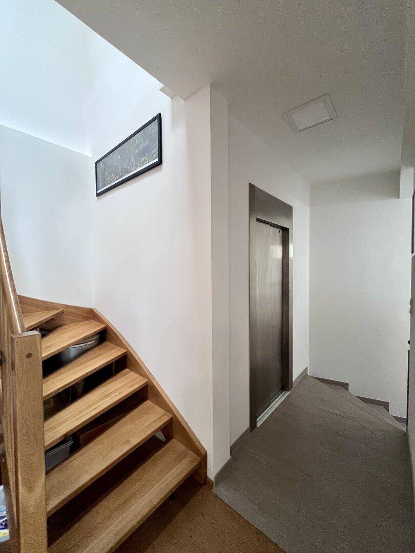 Heller Flur mit Holztreppe und modernem Aufzug, der die verschiedenen Etagen verbindet.