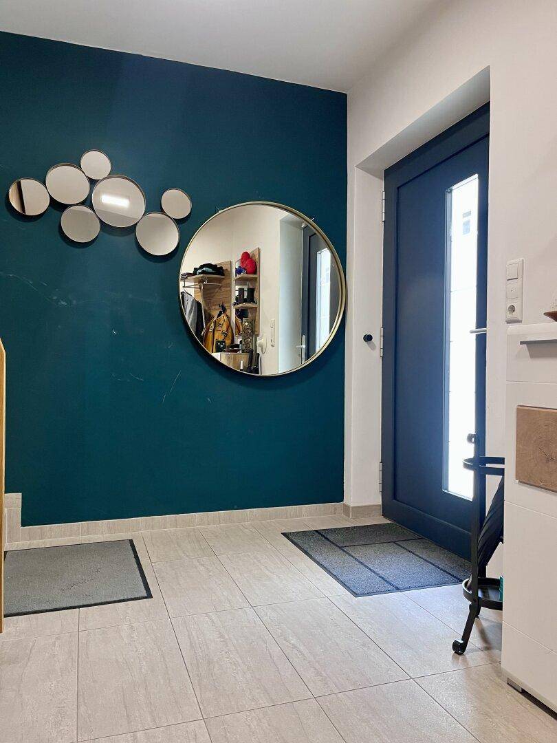 Moderner Eingangsbereich mit einer auffälligen dunkelblauen Wand, dekorativen Spiegeln und Fliesenboden.
