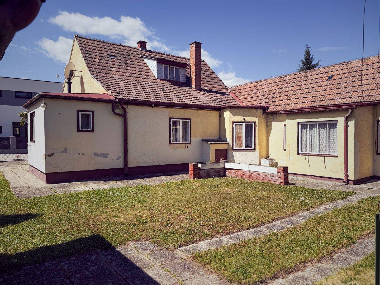 Rückansicht des Hauses mit Gartenfläche und gepflasterten Wegen unter blauem Himmel.