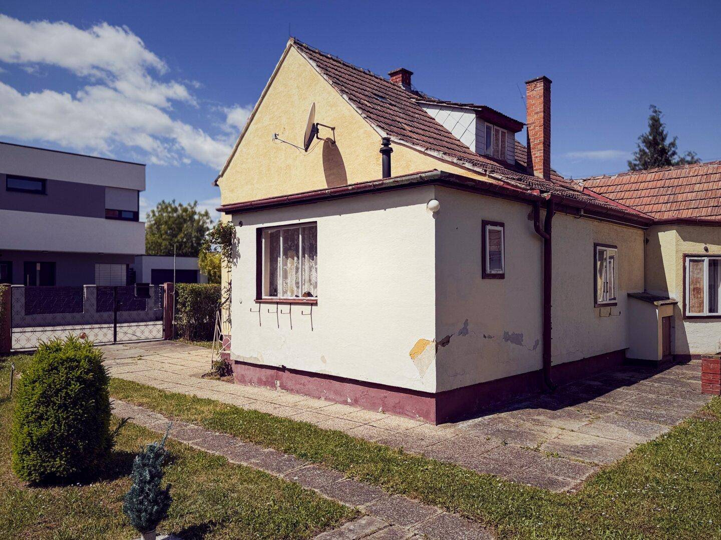 Seitenansicht des Hauses mit gepflastertem Zugang und einem kleinen Busch im Vorgarten.