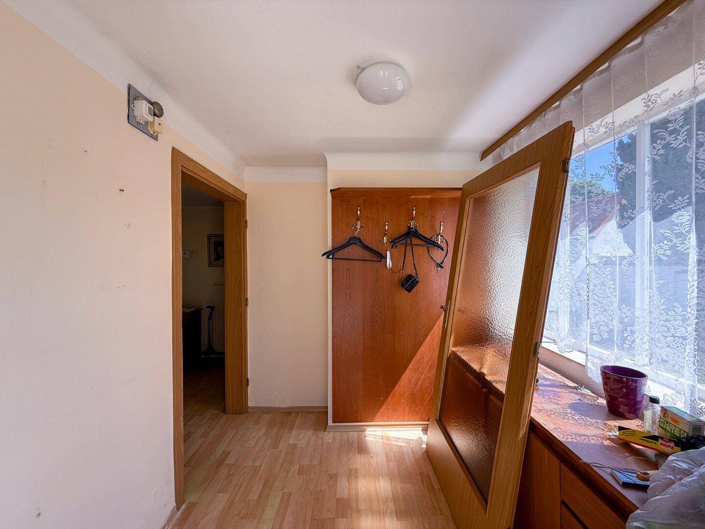 Heller Eingangsbereich mit Garderobe, Holzfußboden und Fenster mit Vorhängen.