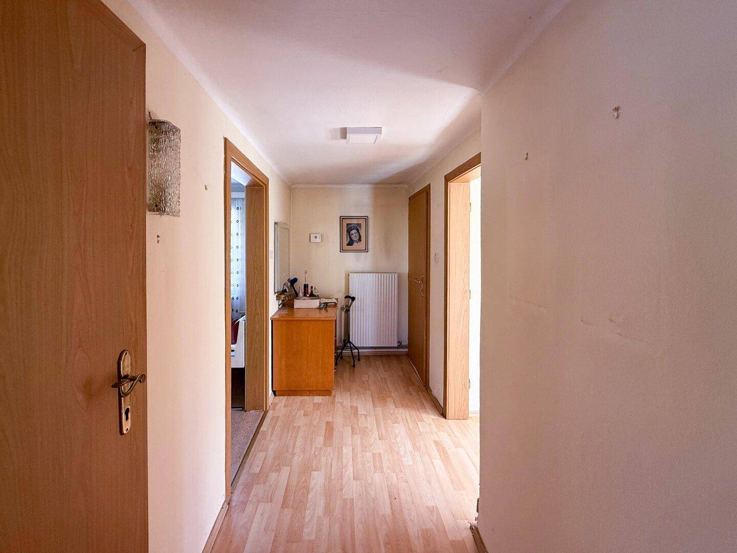 Langer Flur mit Laminatboden, mehreren Türen und einem Heizkörper an der Wand.