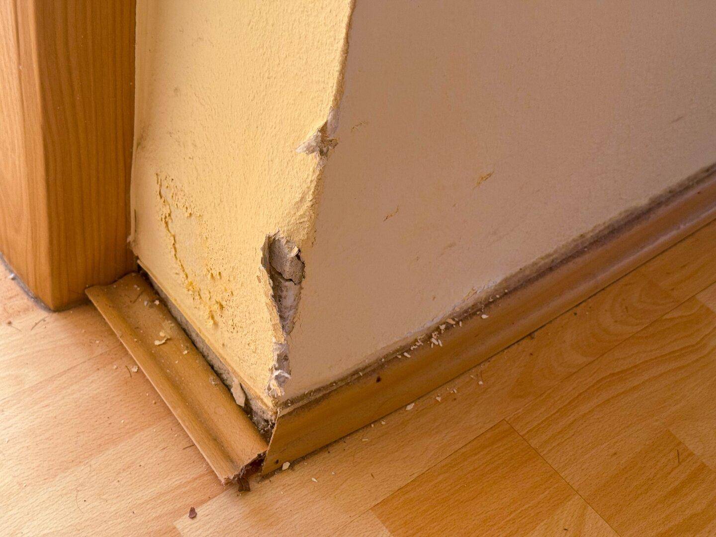 Nahaufnahme einer beschädigten Wand und des Fußbodens, die Renovierungsbedarf zeigen.
