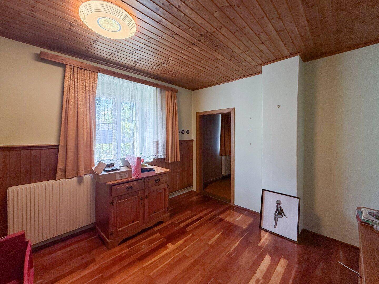 Zimmer mit Holzdielenboden, Holzdecke und Fenster, das Renovierungsbedarf aufweist.