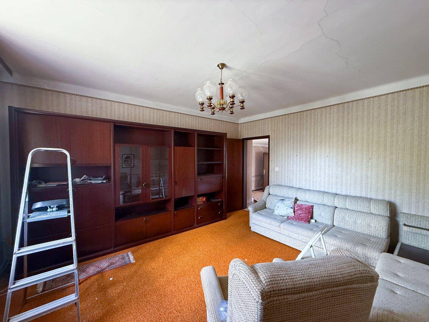Wohnzimmer mit orangefarbenem Teppich, großem Schrank und Sofa, das Renovierung benötigt.