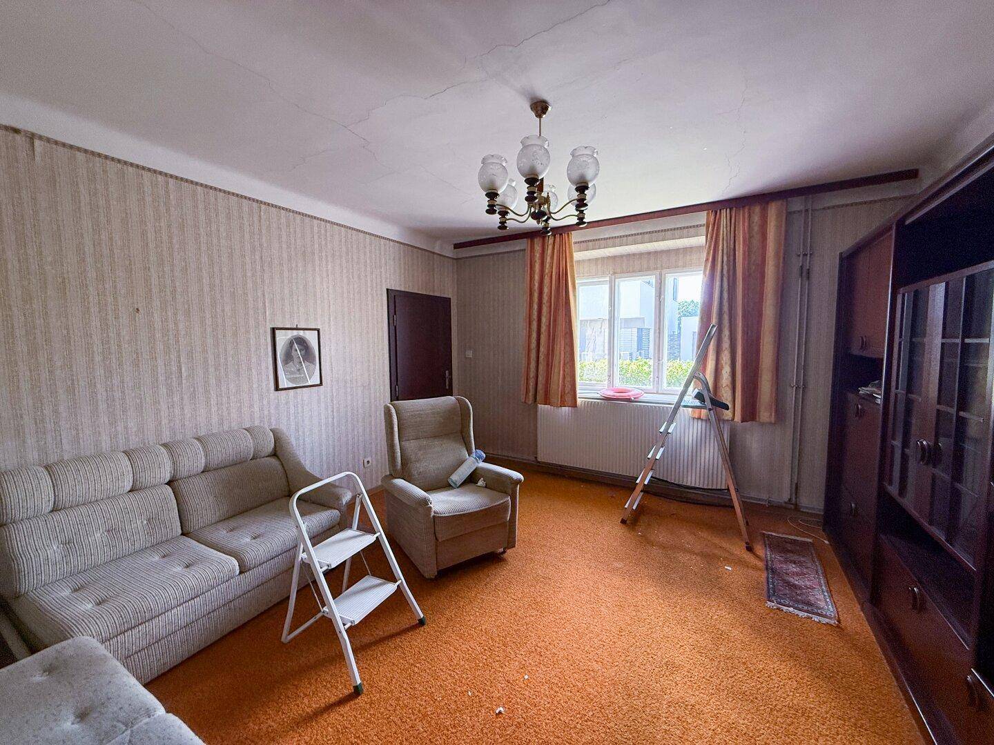 Wohnzimmer mit Teppichboden, Sofa und Sessel, das auf eine Renovierung wartet.