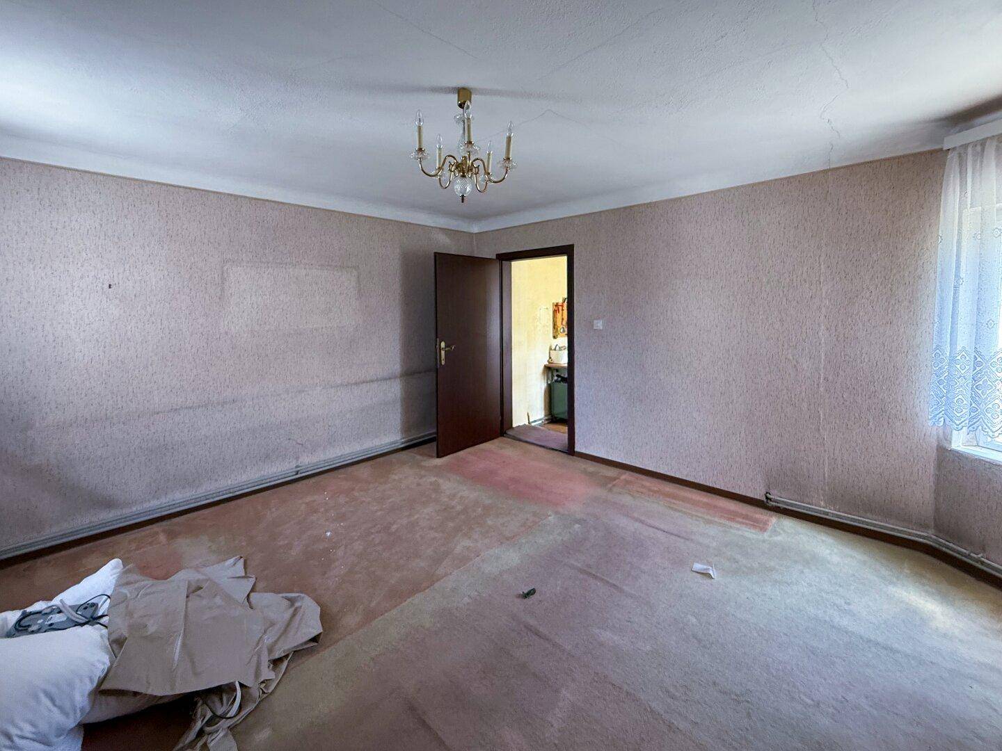 Leeres Zimmer mit Teppichboden und Fenster, bereit für eine umfassende Renovierung.