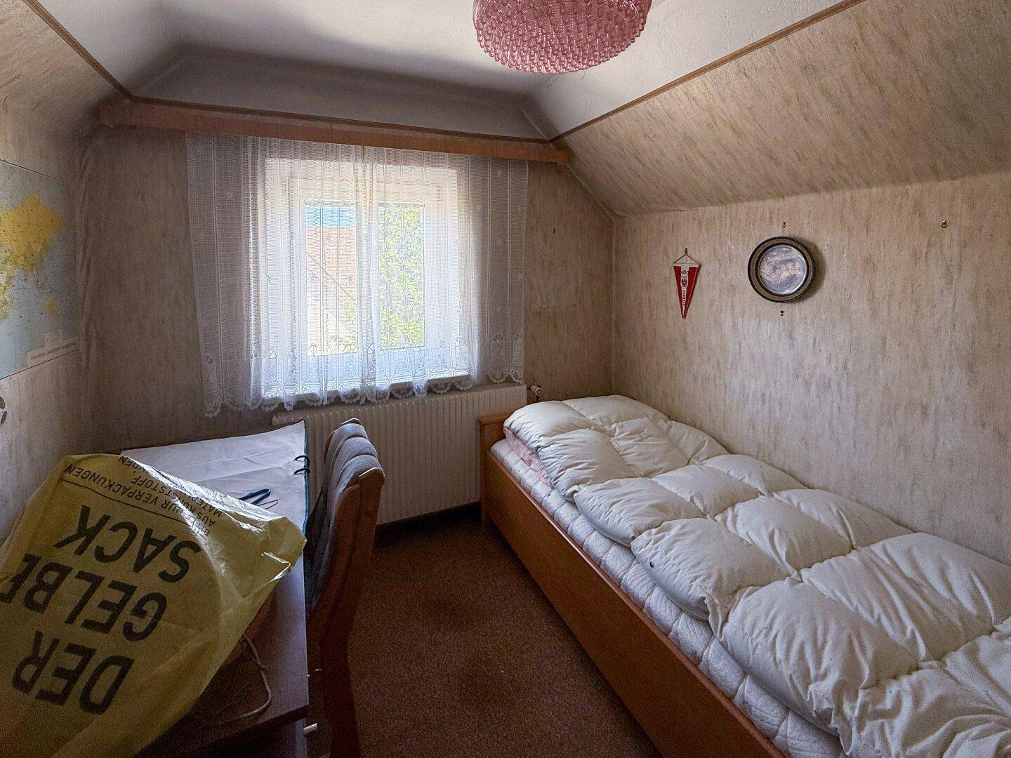 Kleines Schlafzimmer mit Einzelbett, Dachschräge und Fenster, das Renovierung benötigt.
