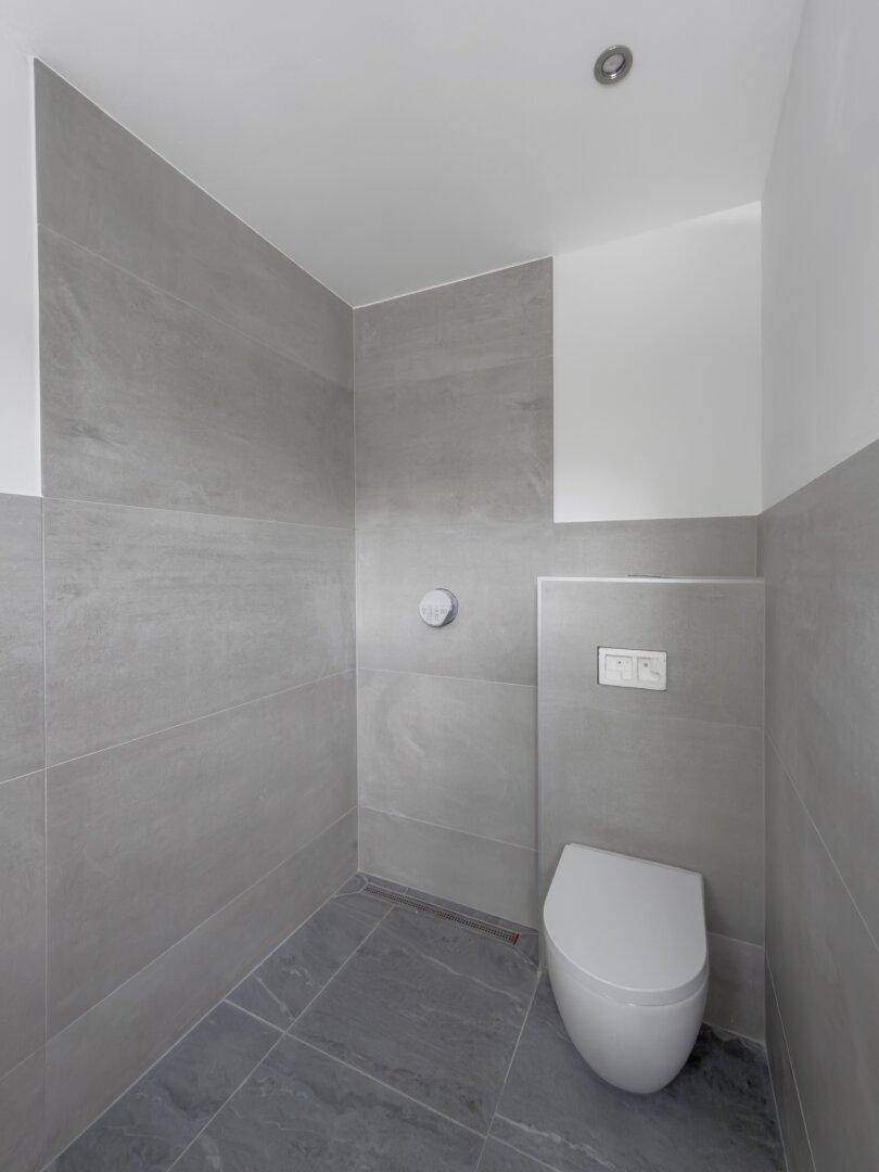 Modernes Gäste-WC mit grauen Fliesen und wandhängendem WC.