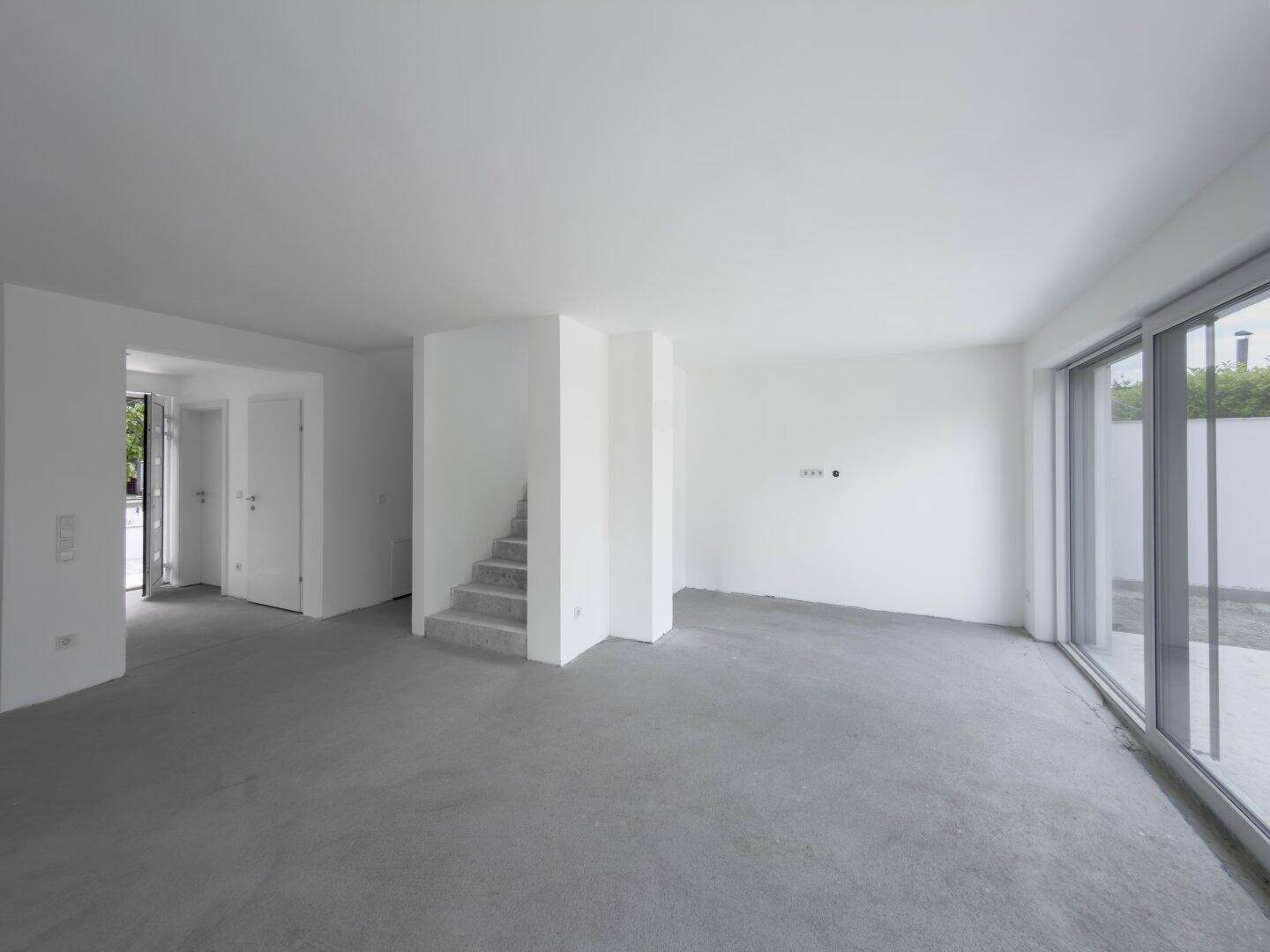 Geräumiger, unfertiger Wohnbereich mit großen Schiebetüren zur Terrasse und Treppenaufgang.