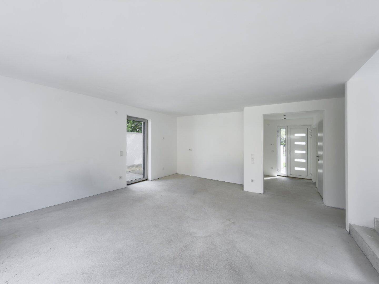 Heller, unfertiger Wohnraum mit Zugang zum Garten und Eingangsbereich.