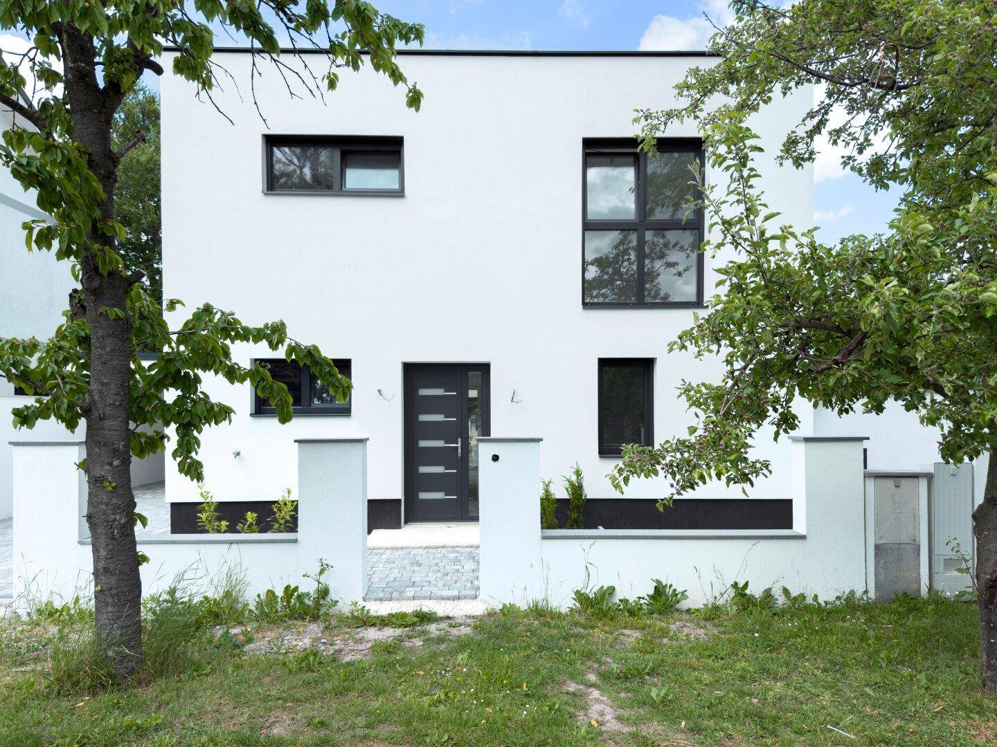 Vorderansicht eines modernen Einfamilienhauses mit weißer Fassade und dunkler Eingangstür.