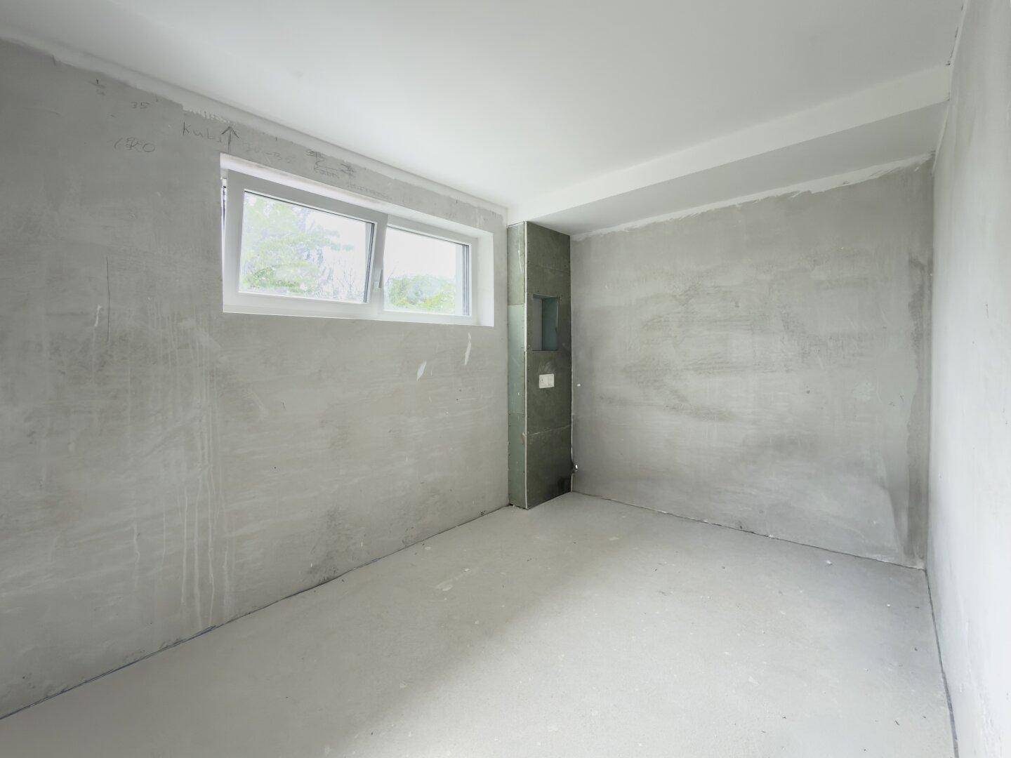Unfertiges Badezimmer mit Fenster und vorbereiteten Anschlüssen für Sanitärobjekte.