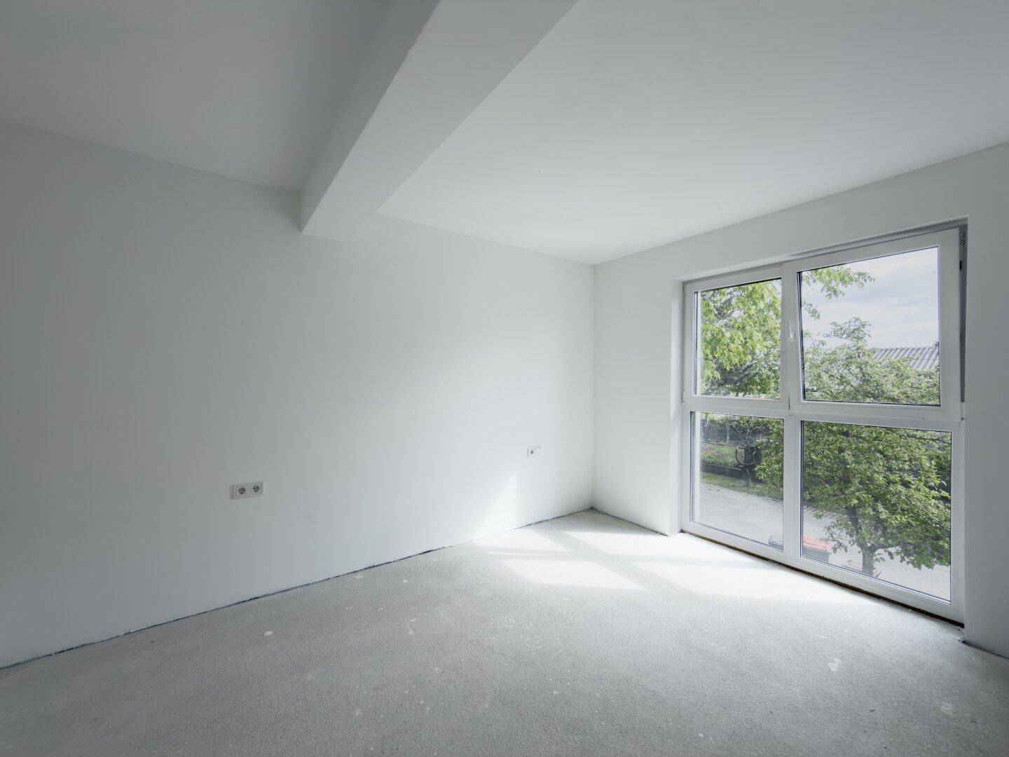 Geräumiges, unfertiges Zimmer mit großer Fensterfront und Blick auf Bäume.