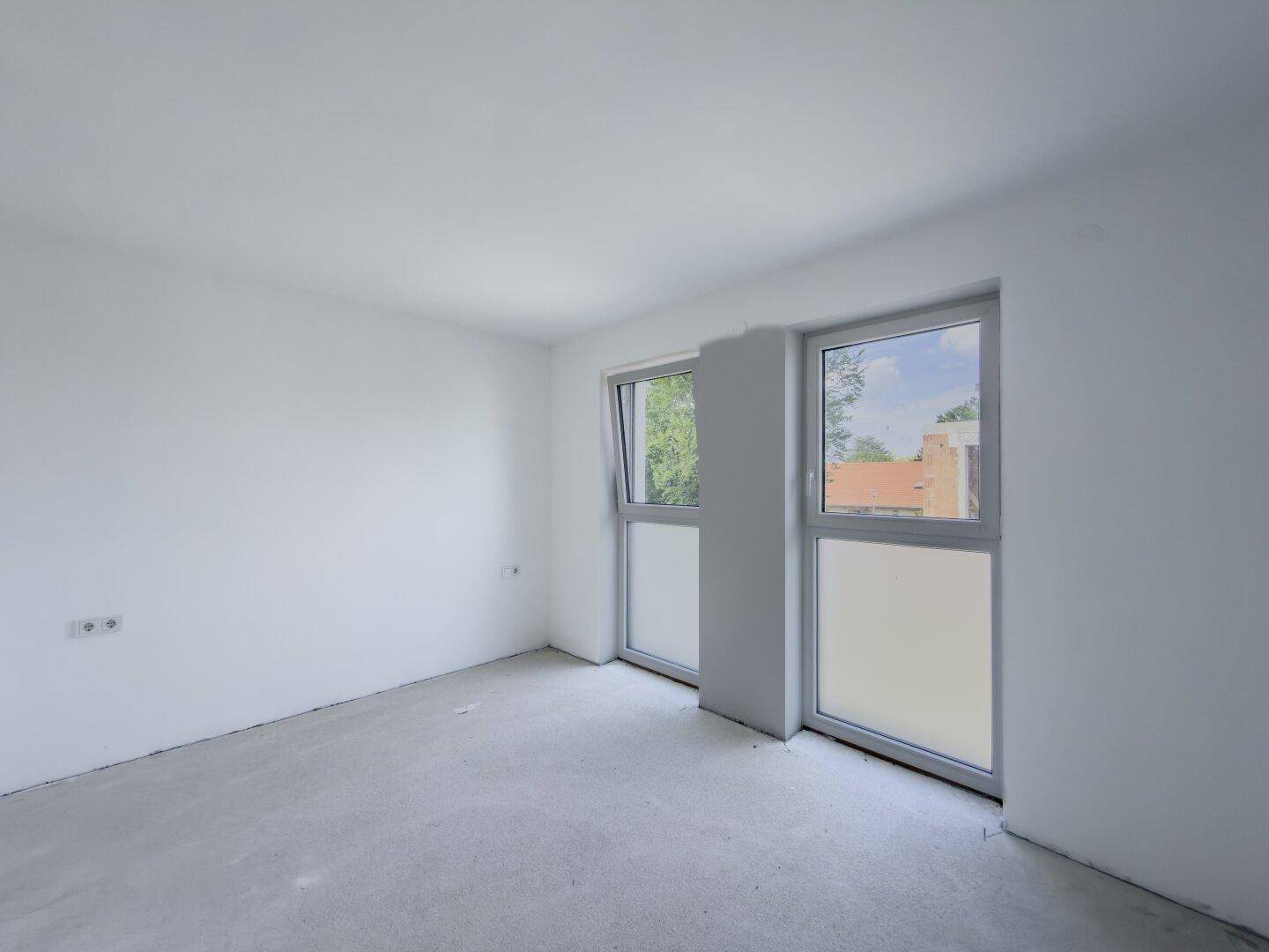 Helles, unfertiges Zimmer mit großen Fenstern und Blick ins Grüne.