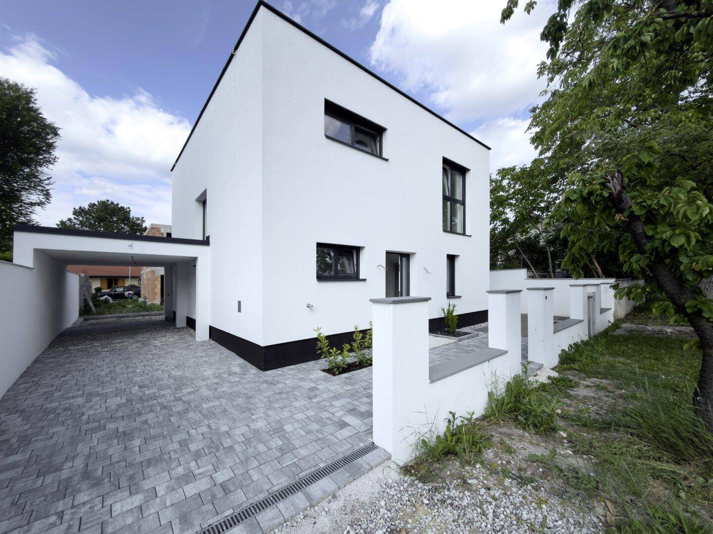 Seitenansicht des modernen Hauses mit Carport und gepflasterter Zufahrt.