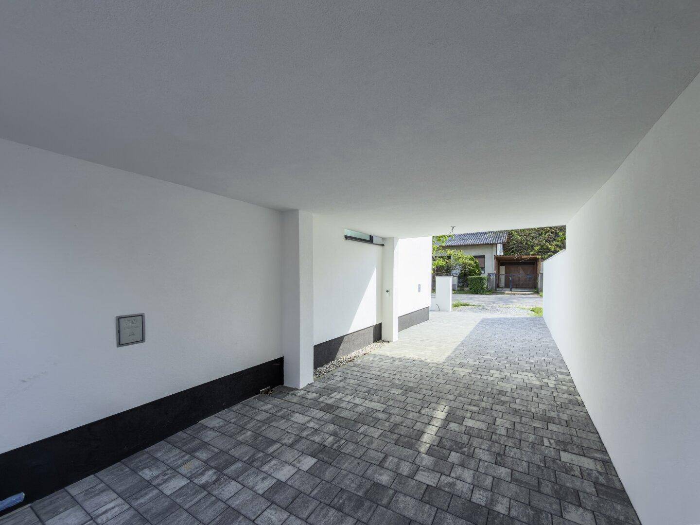 Überdachter Stellplatz mit gepflastertem Boden und direktem Zugang zum Haus.