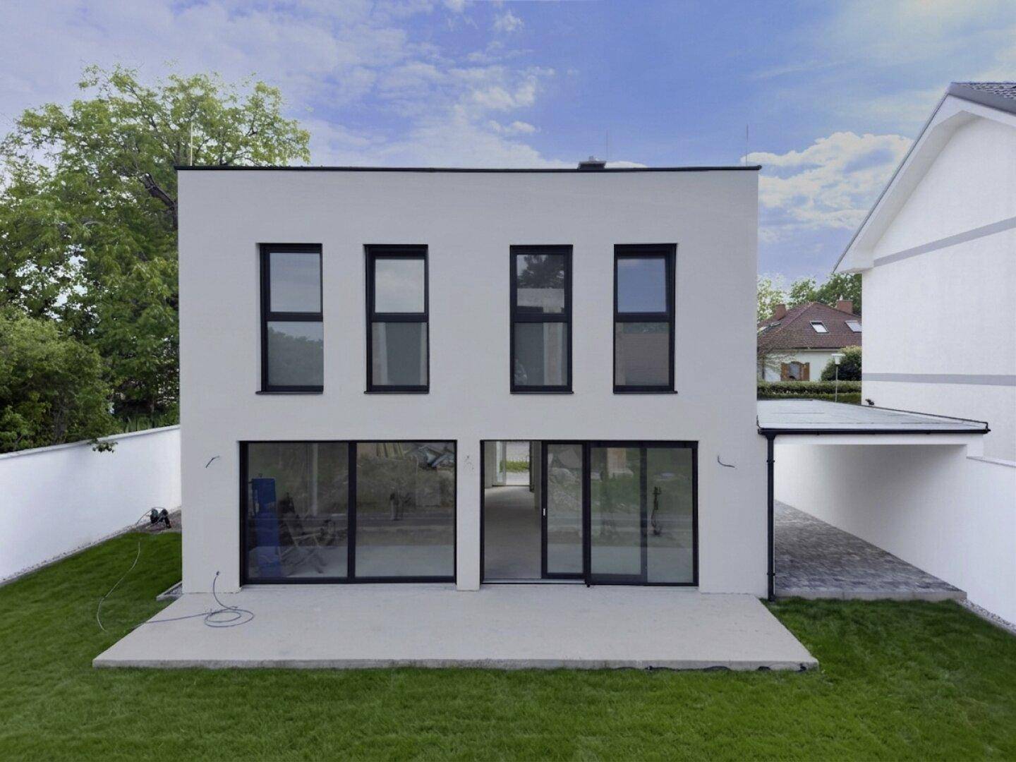 Rückansicht des modernen Hauses mit großen Fensterfronten und Zugang zum Garten.