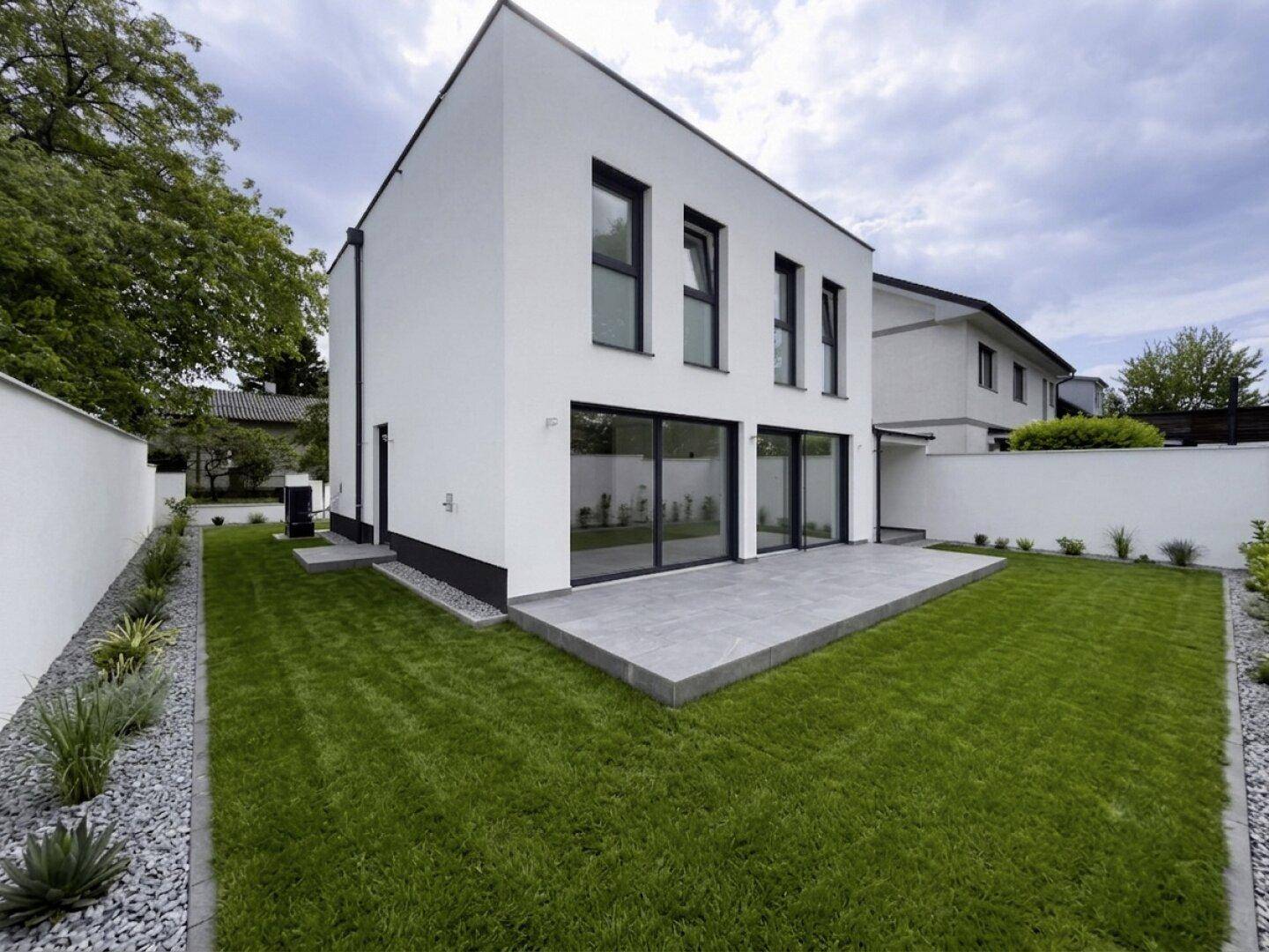Rückseite eines modernen Hauses mit großer Terrasse und weitläufigem, gepflegtem Gartenbereich.