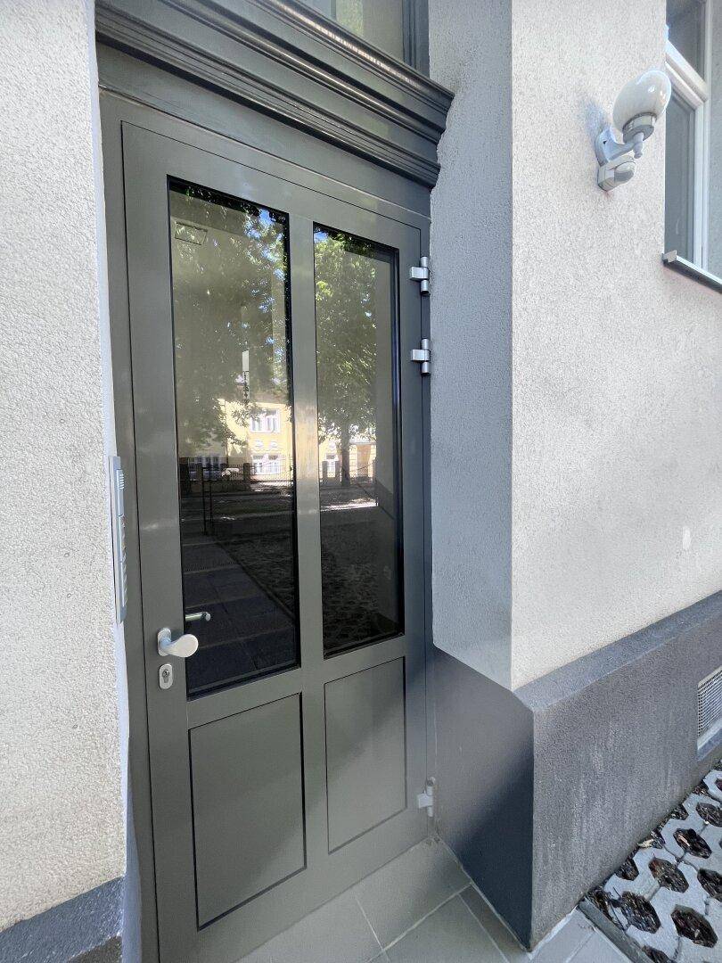 Moderne graue Eingangstür mit Glaseinsätzen und einem klassischen, verzierten Rahmen.