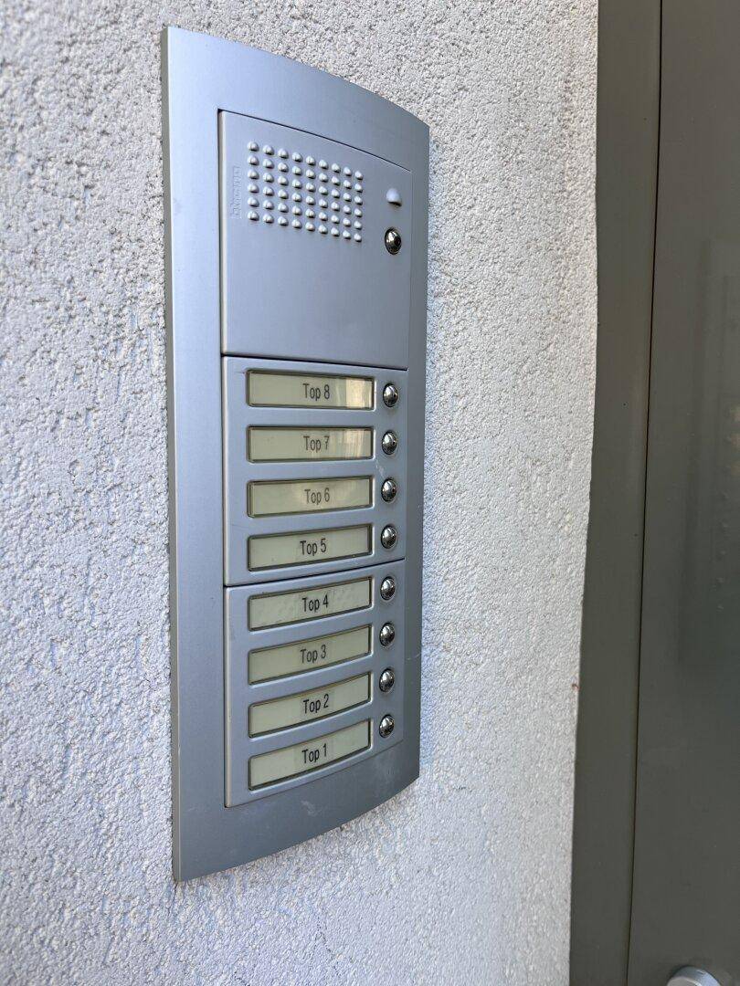 Silberne Gegensprechanlage mit mehreren Klingelknöpfen für verschiedene Wohneinheiten am Eingang.