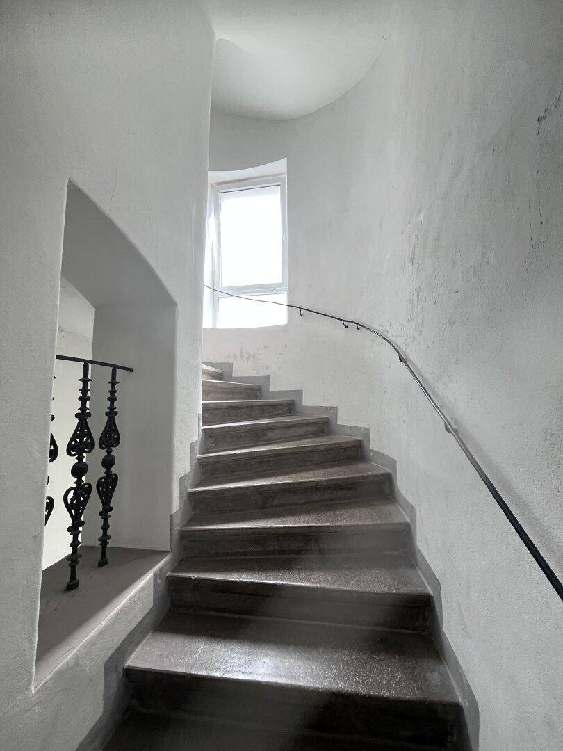 Historisches Treppenhaus mit einer Wendeltreppe aus Stein und einem schmiedeeisernen Geländer.