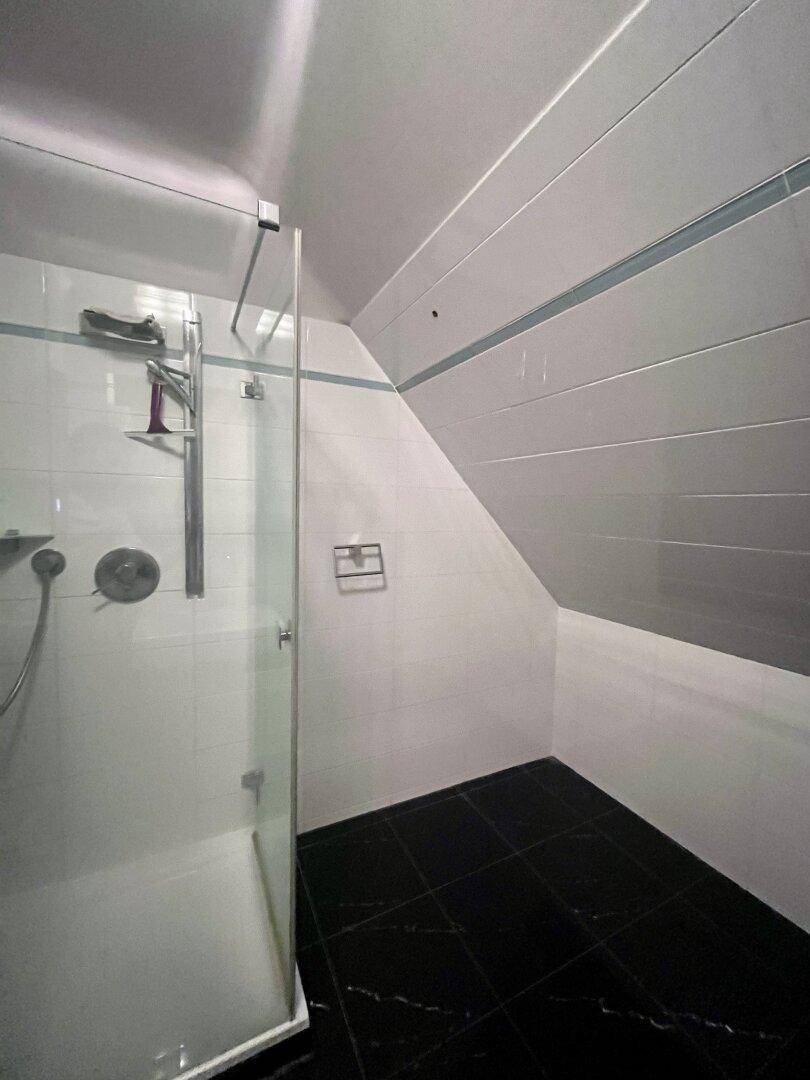 Modernes Badezimmer mit Duschkabine, weißen Wandfliesen und dunklem Boden im Dachgeschoss.