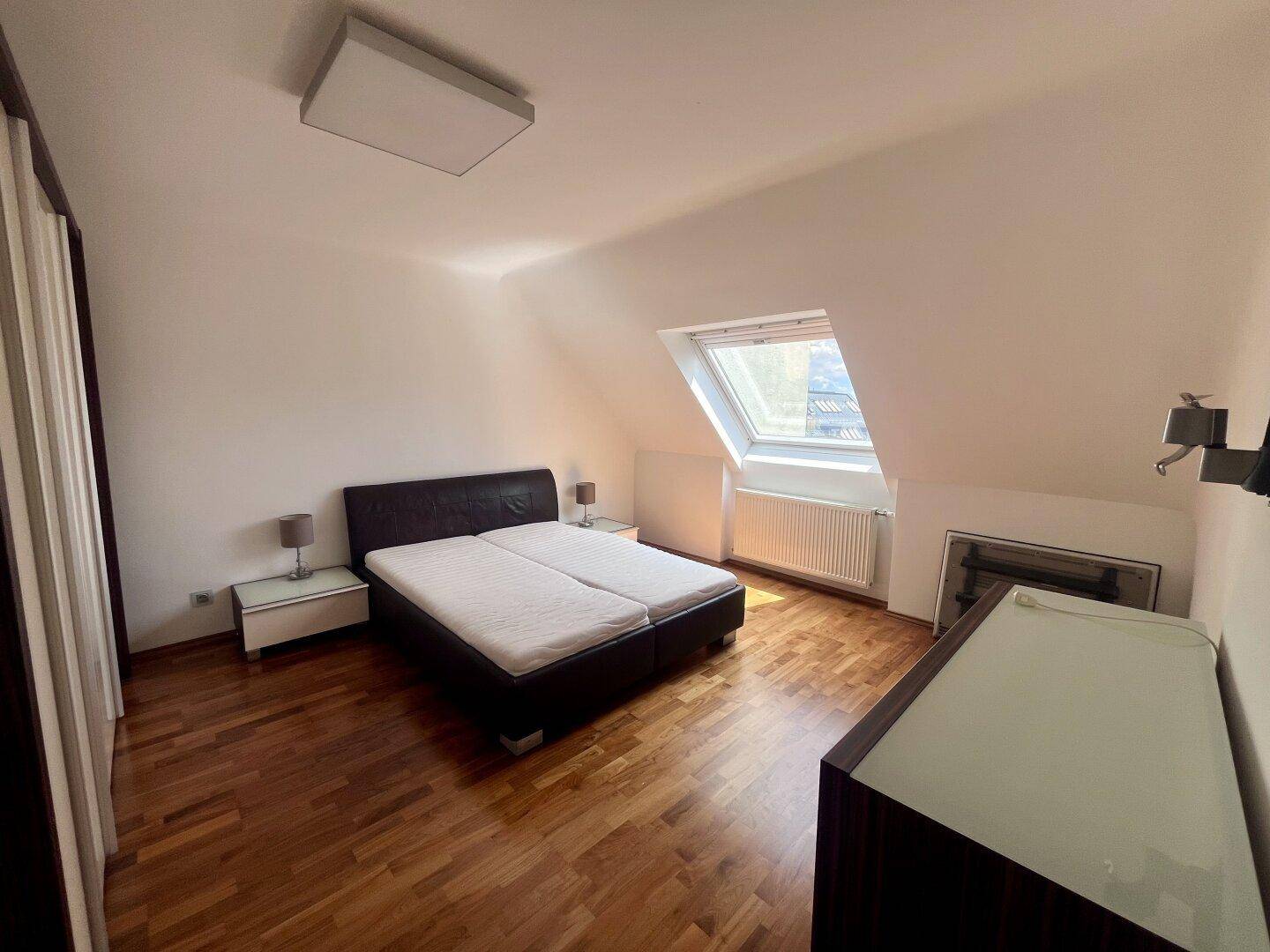 Gemütliches Schlafzimmer im Dachgeschoss mit Doppelbett, Holzboden und einem Dachfenster.