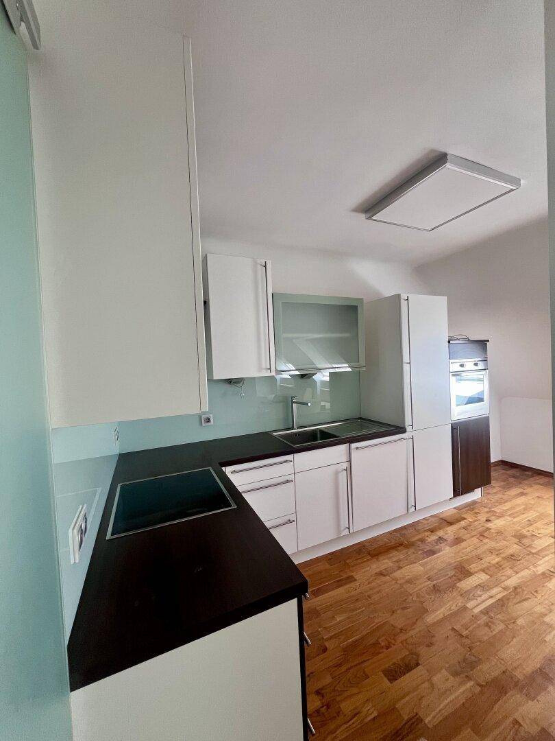 Funktionale Küche mit weißen Schränken, dunkler Arbeitsplatte, Induktionskochfeld und integriertem Backofen.