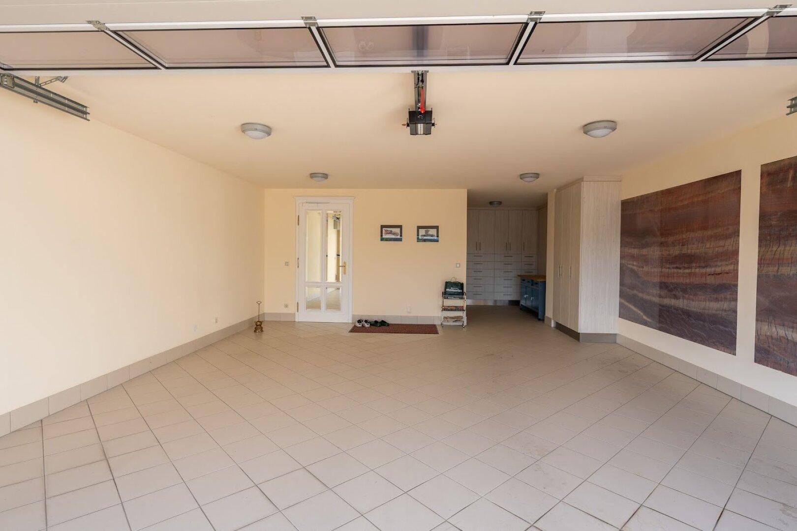 Geräumige Garage mit Fliesenboden, Rolltor und Zugang zu weiteren Räumen.