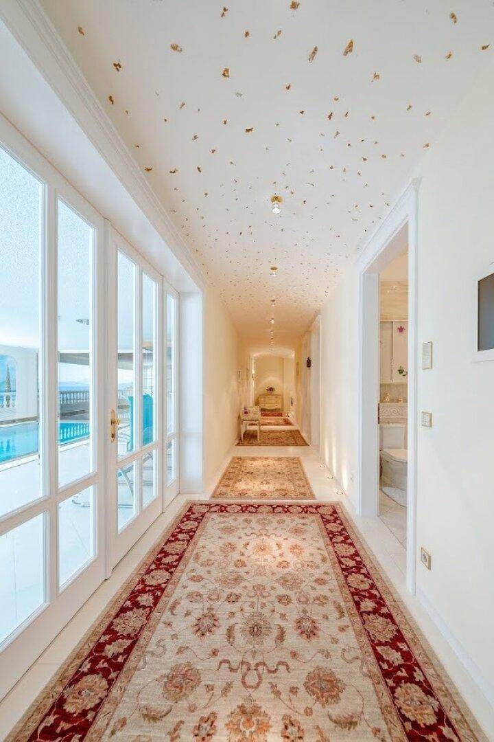 Heller Flur mit Teppichen und dekorativer Decke, der zum luxuriösen Poolbereich führt.