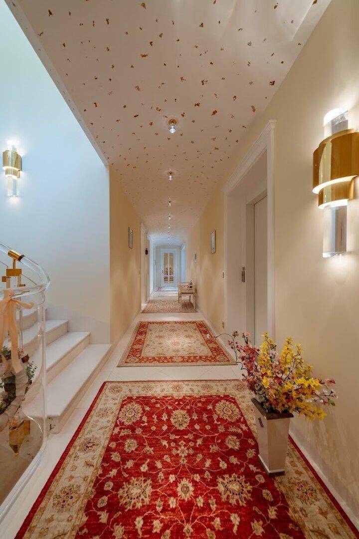 Eleganter Treppenaufgang und Flur mit Teppichen, Wandleuchten und dekorativer Decke.