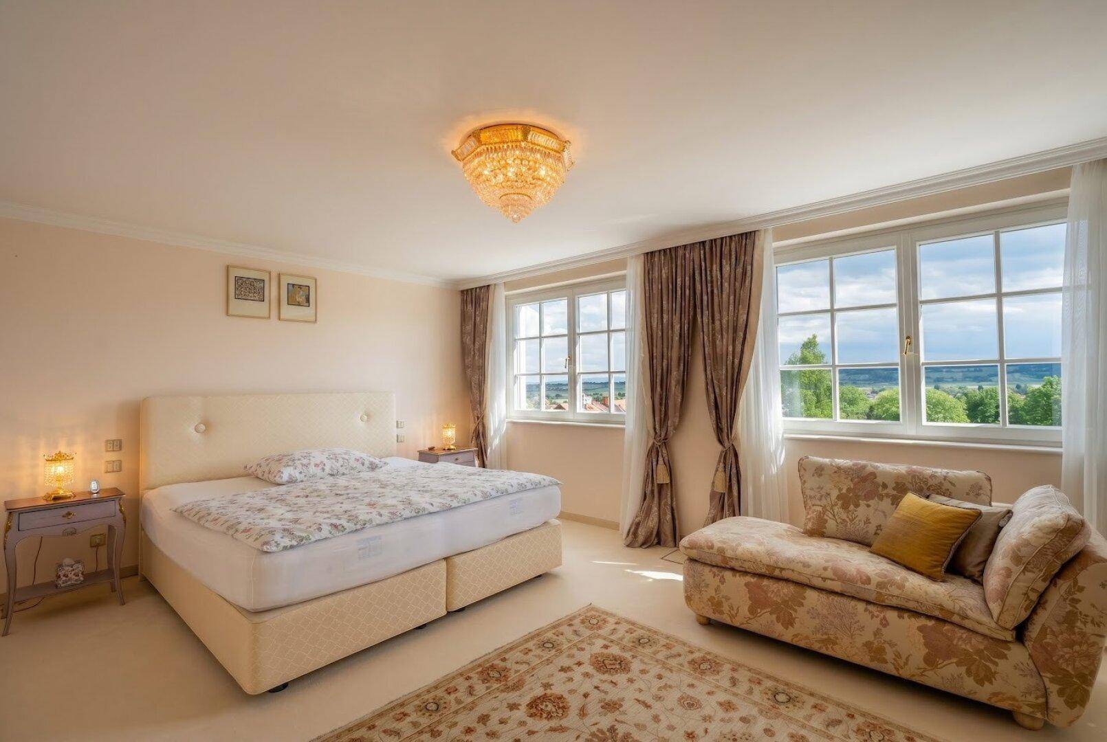 Helles Schlafzimmer mit Doppelbett, bequemer Chaiselongue und weitem Blick in die Landschaft.
