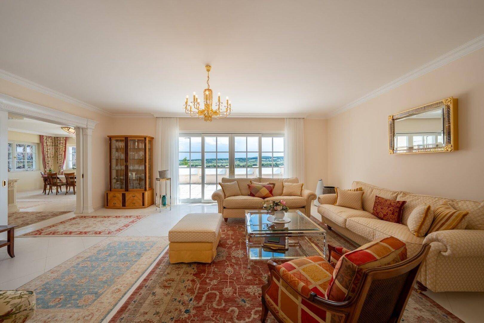 Geräumiges Wohnzimmer mit klassischem Mobiliar, Kronleuchter und Zugang zu einem Balkon mit Aussicht.