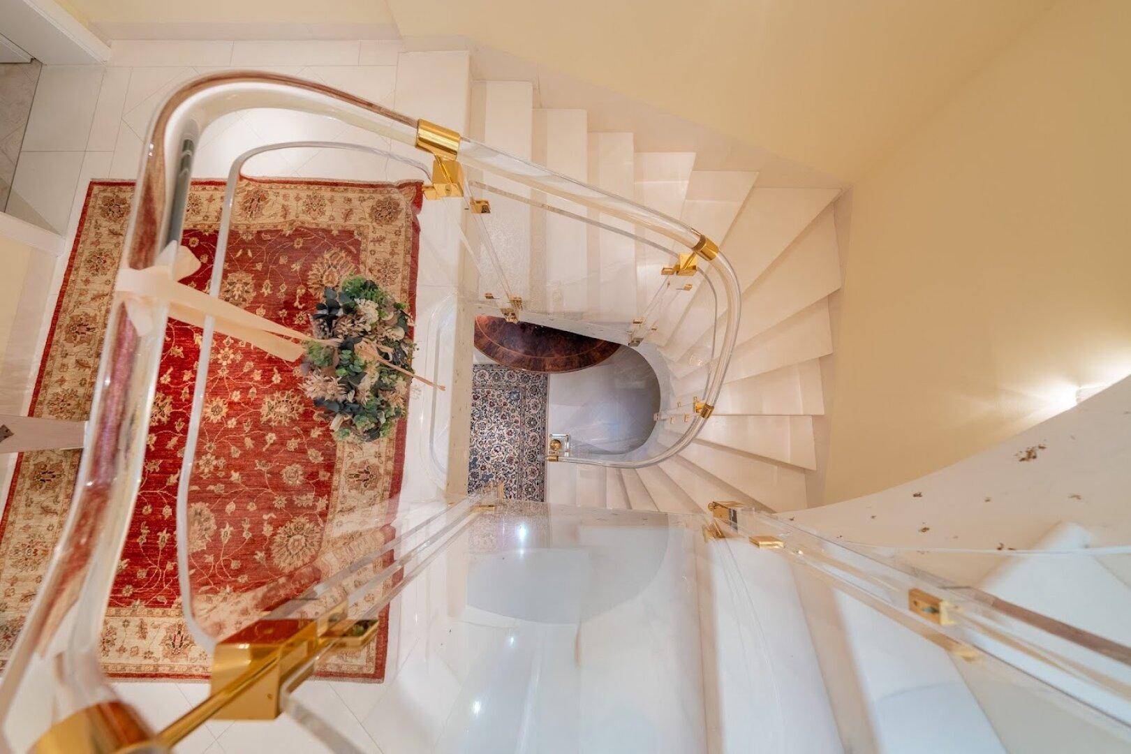 Elegante Wendeltreppe mit transparentem Geländer und Teppichboden, die die Etagen verbindet.