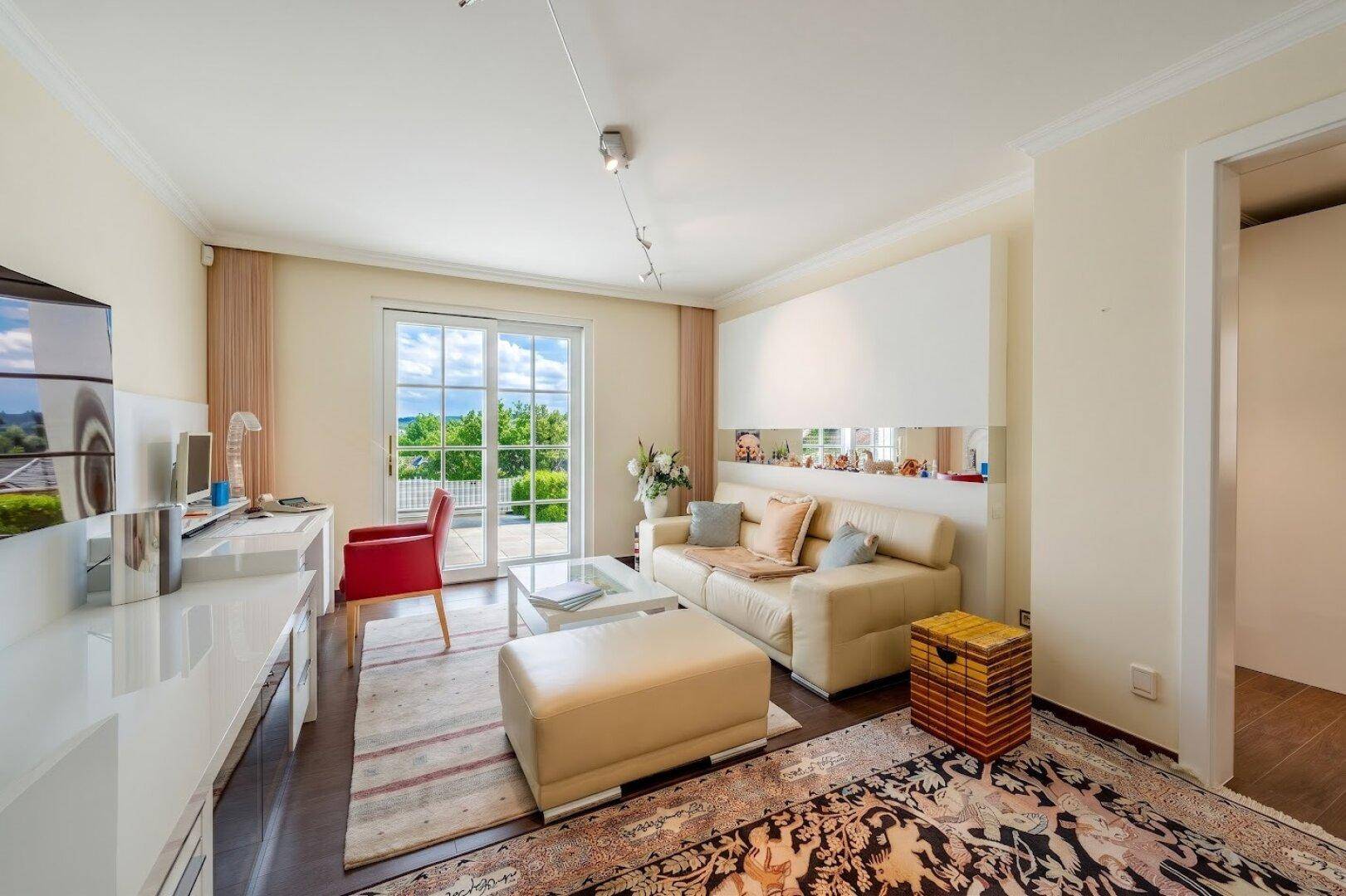 Helles Wohnzimmer mit Sofa, Schreibtisch und Zugang zu einem Balkon mit schöner Aussicht.