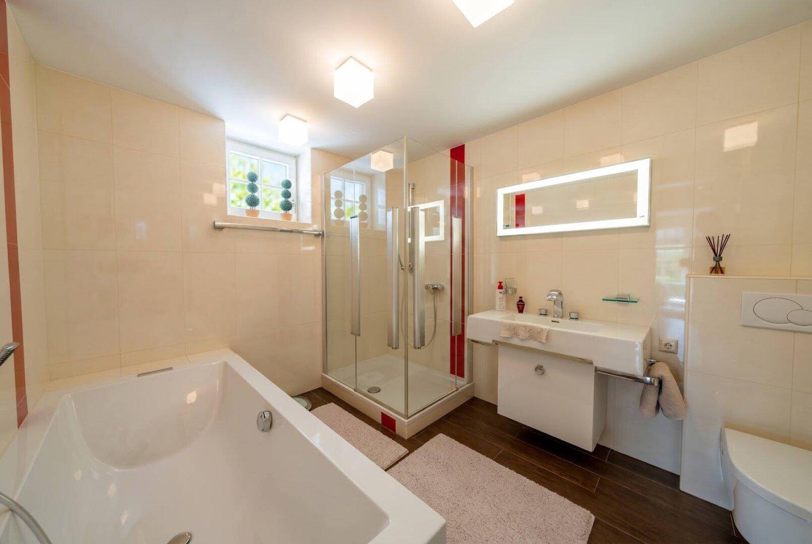 Helles Badezimmer mit Badewanne, Duschkabine, modernem Waschtisch und Fenster.