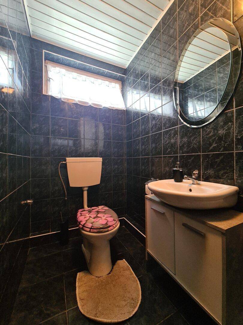 Kleines WC mit dunklen Fliesen, Waschbecken und einem Fenster für Tageslicht.