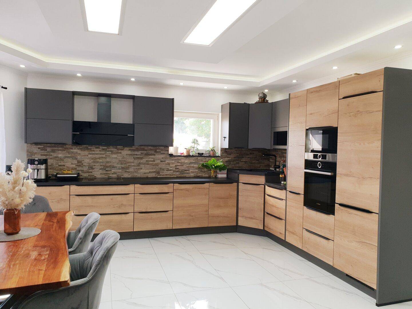 Moderne Einbauküche mit Holz- und grauen Fronten, schwarzen Arbeitsplatten und integrierten Geräten.