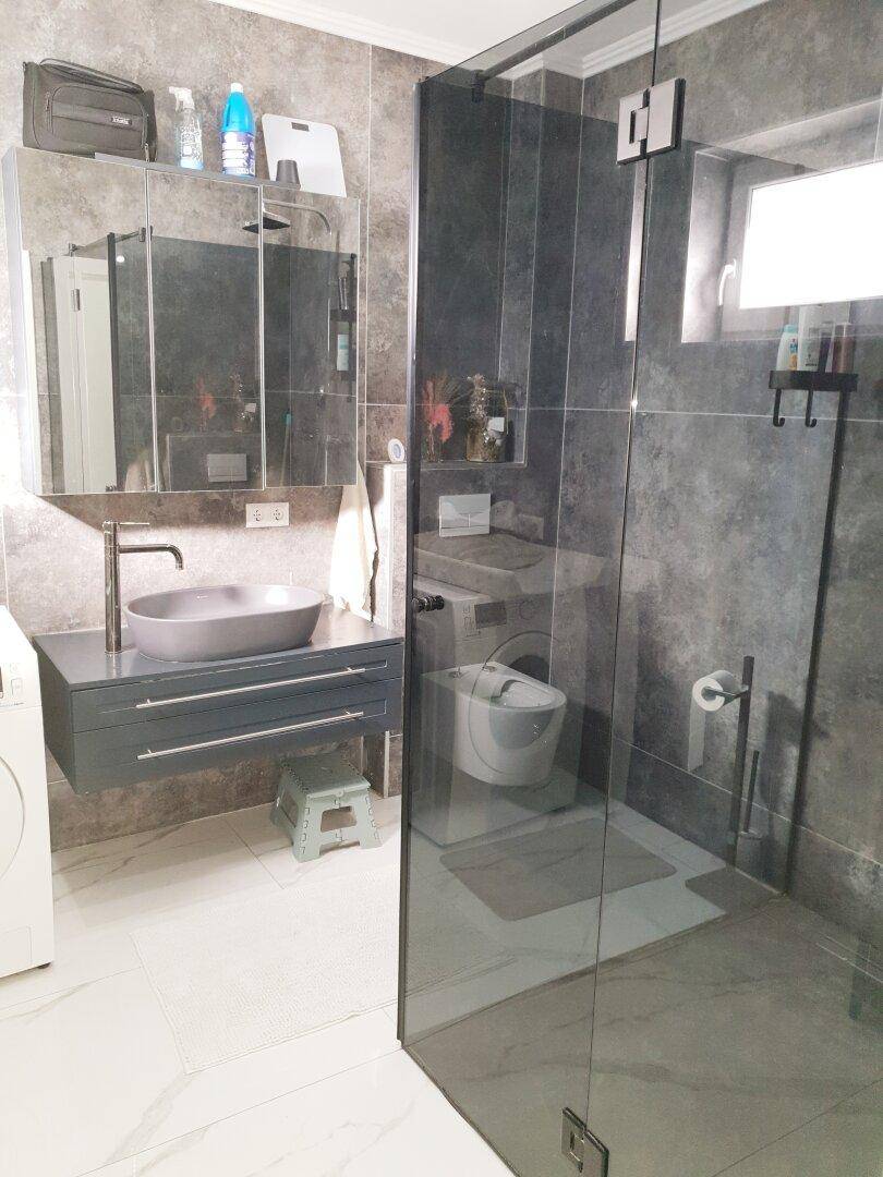 Modernes Badezimmer mit grauen Fliesen, begehbarer Dusche und schwebendem Waschtisch.