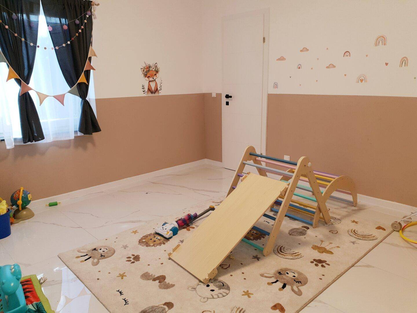 Kinderzimmer mit Spielgeräten, zweifarbigen Wänden und einem Teppich auf Fliesenboden.