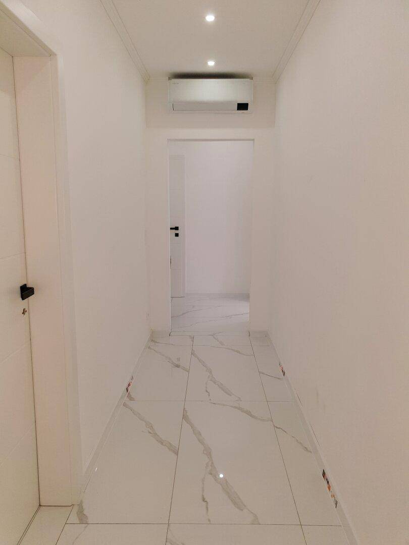 Heller Flur mit modernen Fliesen, Einbaustrahlern und einer Klimaanlage an der Decke.
