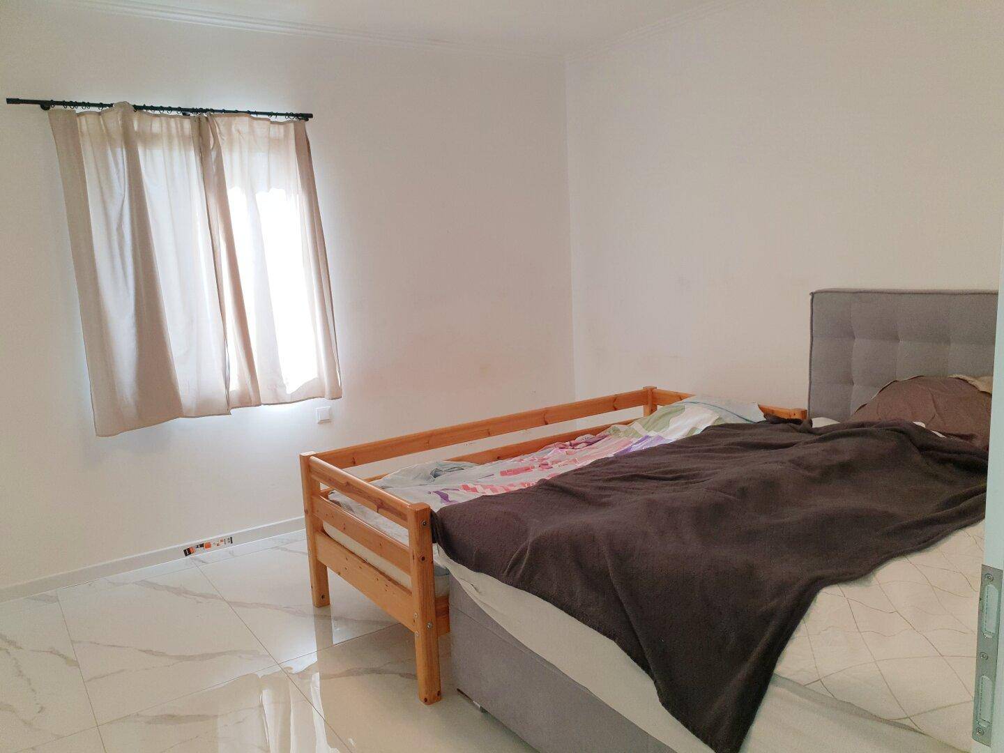 Schlafzimmer mit Bett, weißen Wänden und hellem Fliesenboden.
