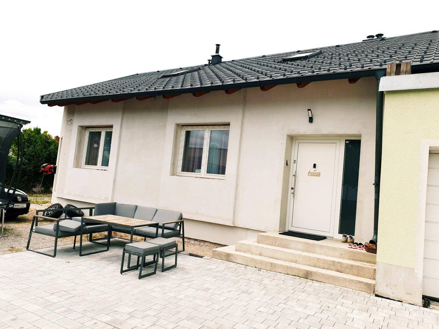Eingangsbereich des Hauses mit gepflasterter Terrasse und moderner Outdoor-Sitzgruppe.