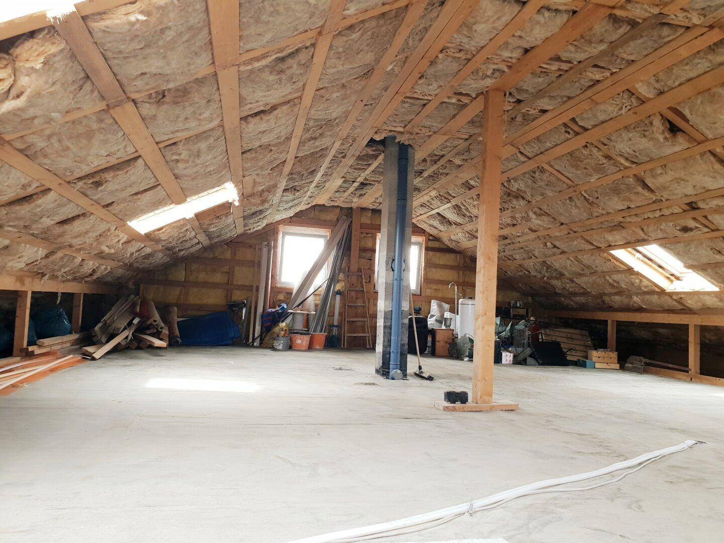 Unfertiger Dachboden mit sichtbaren Holzbalken, Isolierung und Dachfenstern.