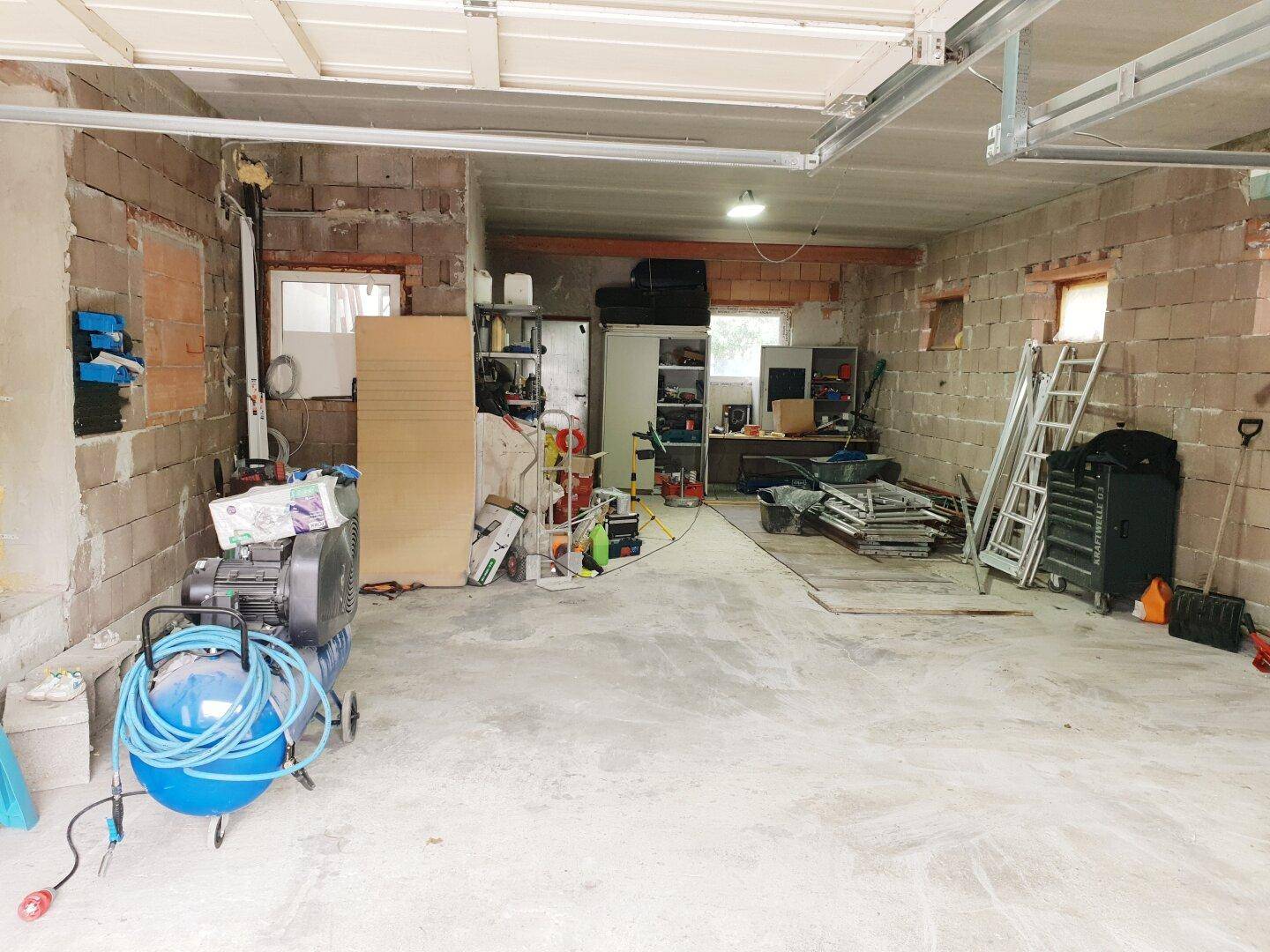 Unfertige Garage mit Betonwänden, Betonboden und verschiedenen Werkzeugen.
