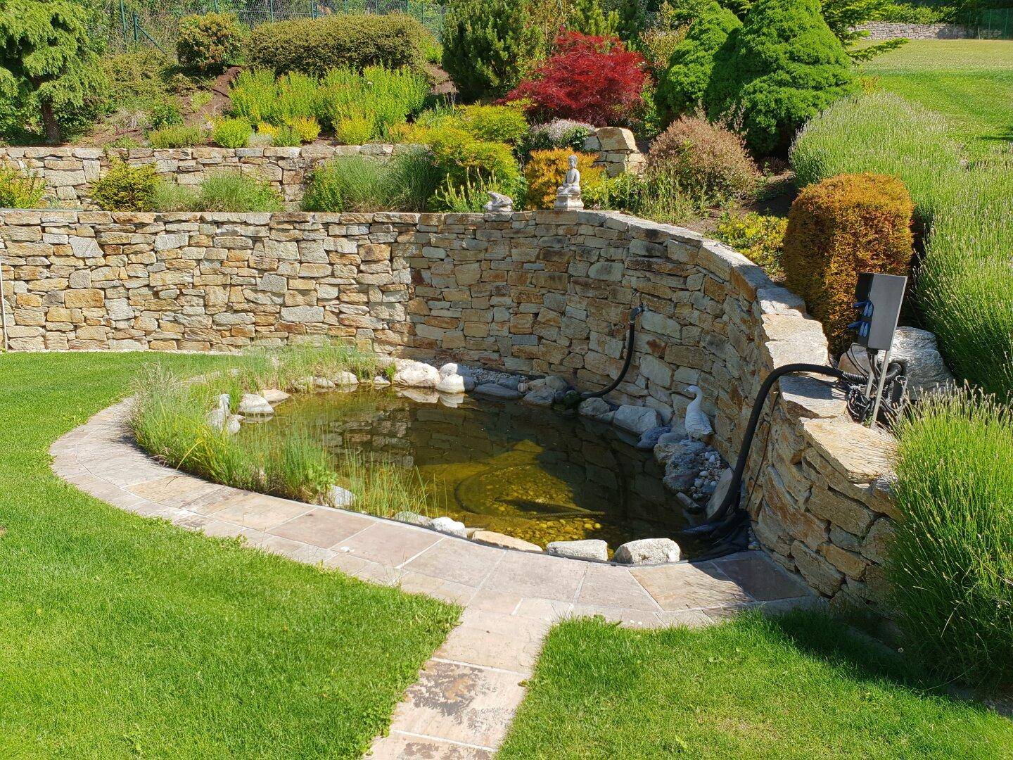 Gepflegter Garten mit Natursteinmauern, Zierpflanzen und einem kleinen Teich.